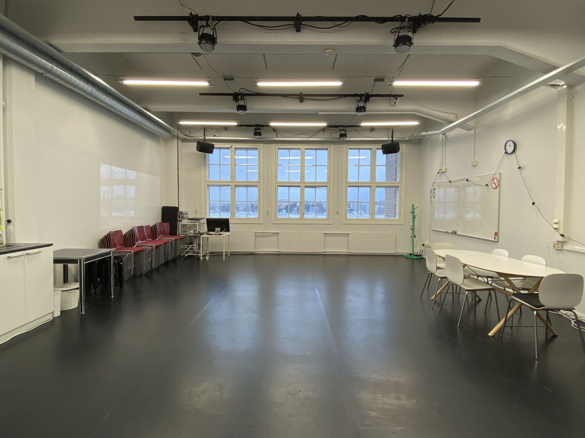 Ett stort rum med dansmatta på golvet. I taket finns både lysrör och lampor för scenbelysning. På den bortre väggen finns stora fönster. På höger sida av rummet syns en whiteboard och ett bord med sex stolar. På vänster sida av rummet finns röda stolar staplade i högar, ett litet bord och i bildens vänstra kant syns hörnet av en diskbänk. Längst bort i vänstra hörnet syns en dator.
