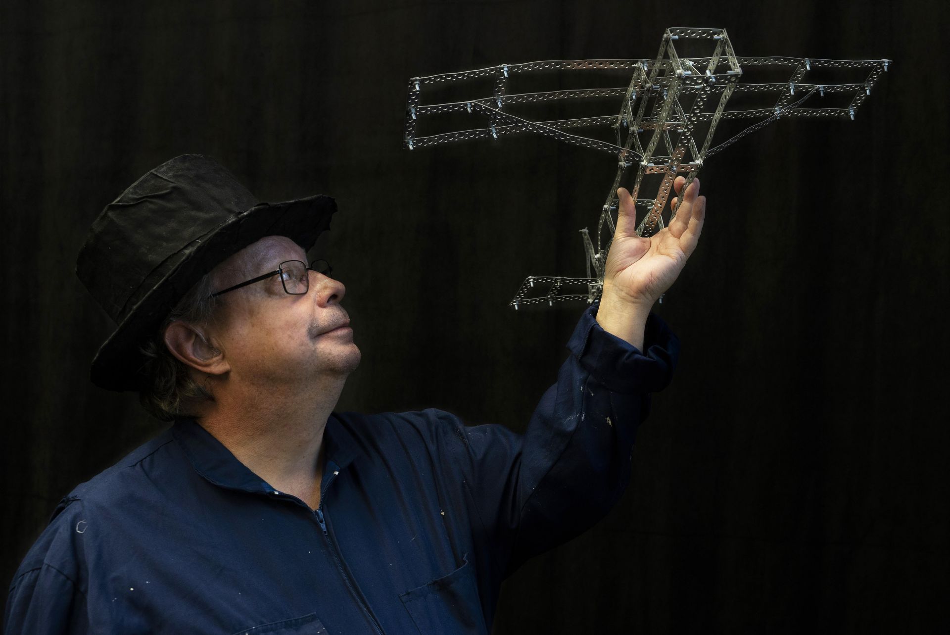 DuvTeatern actor Krister Ekebom with a top hat, looking towards his miniature airplane made of perforated steel banding. 