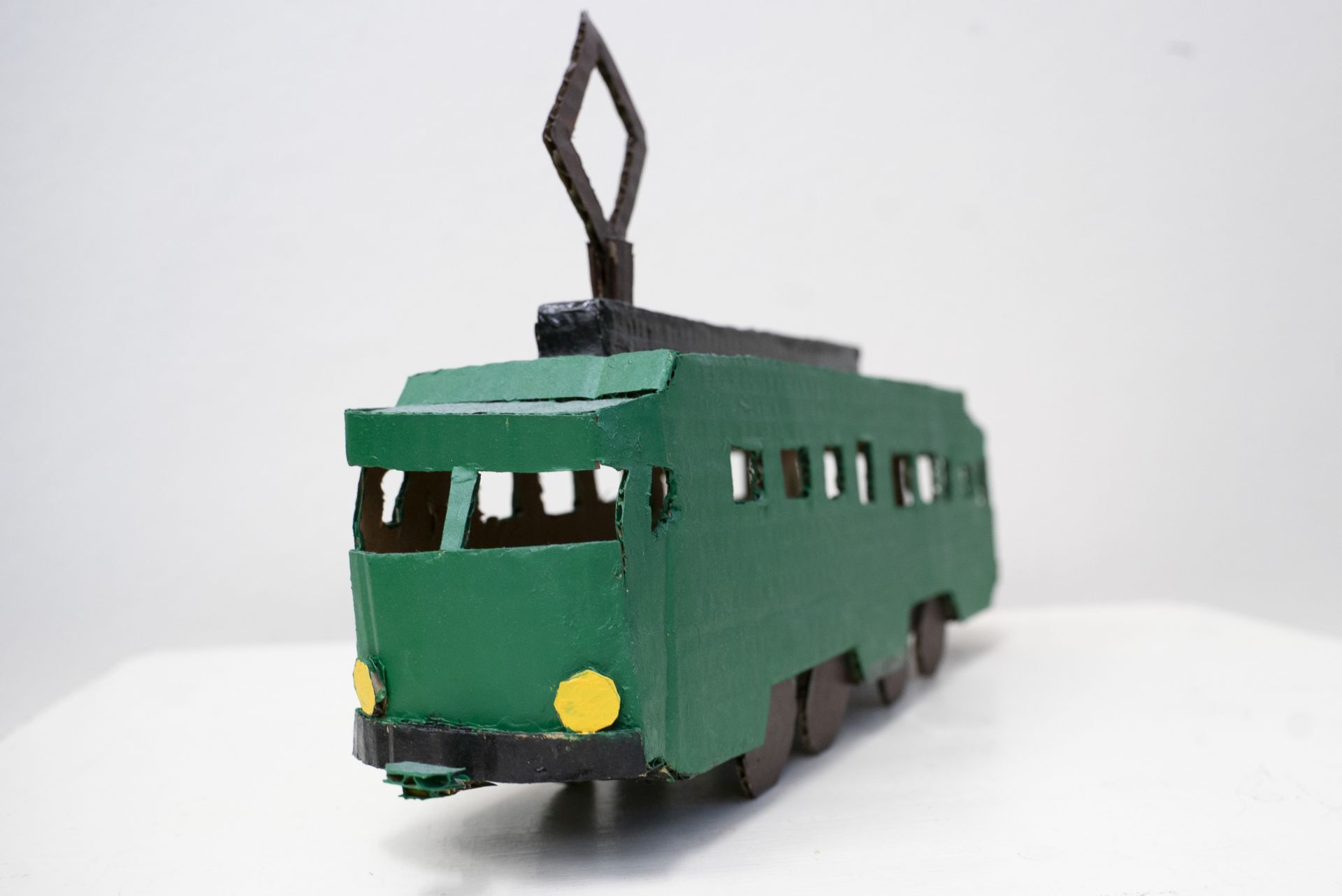 Cardboard miniature of an old tram from Helsinki. The tram is painted dark green with black and yellow details. 