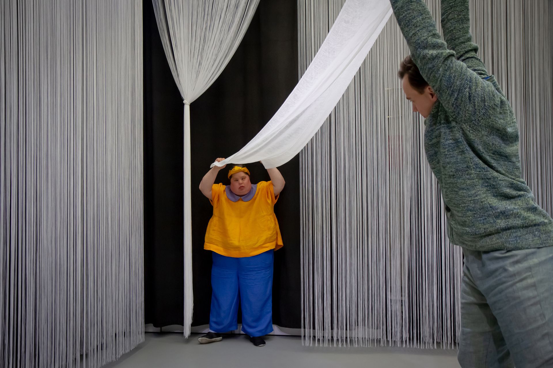 DuvTeatern actress Pia Renes, clad in a brightly colored dancing costume, holds a white sheet with both hands above her head. Dancer Carl Knif holds the other end of the sheet, dressed in more muted colors.